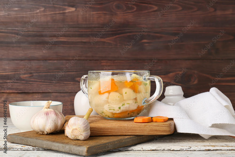 Glass bowl of tasty dumpling soup and garlic on wooden table