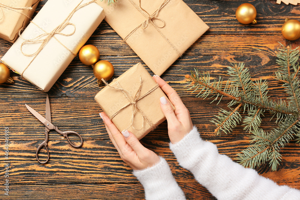 Female hands with Christmas gifts, scissors and decorations on wooden background, closeup