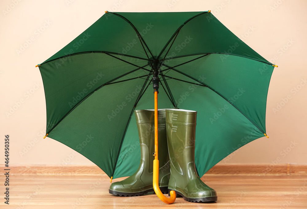 Pair of rubber boots with umbrella near color wall