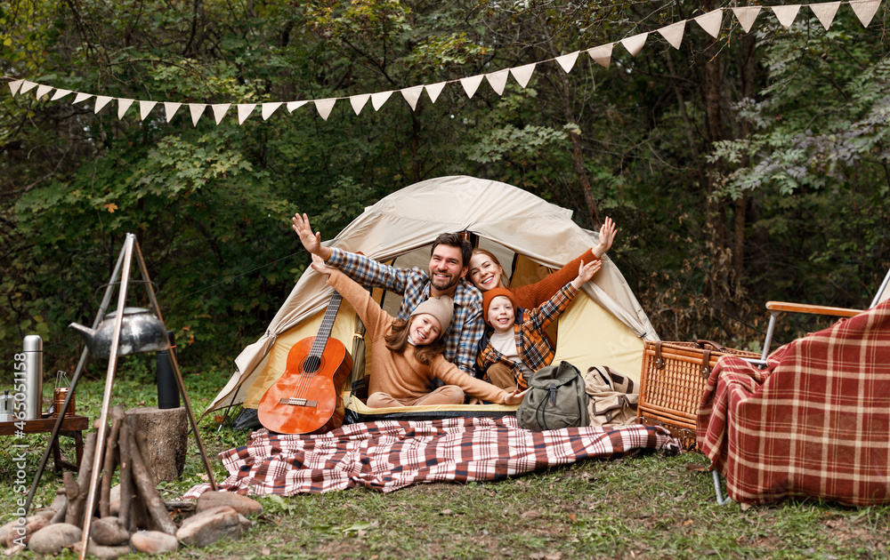 Happy family father, mother and two little children sitting in tent at campsite in forest