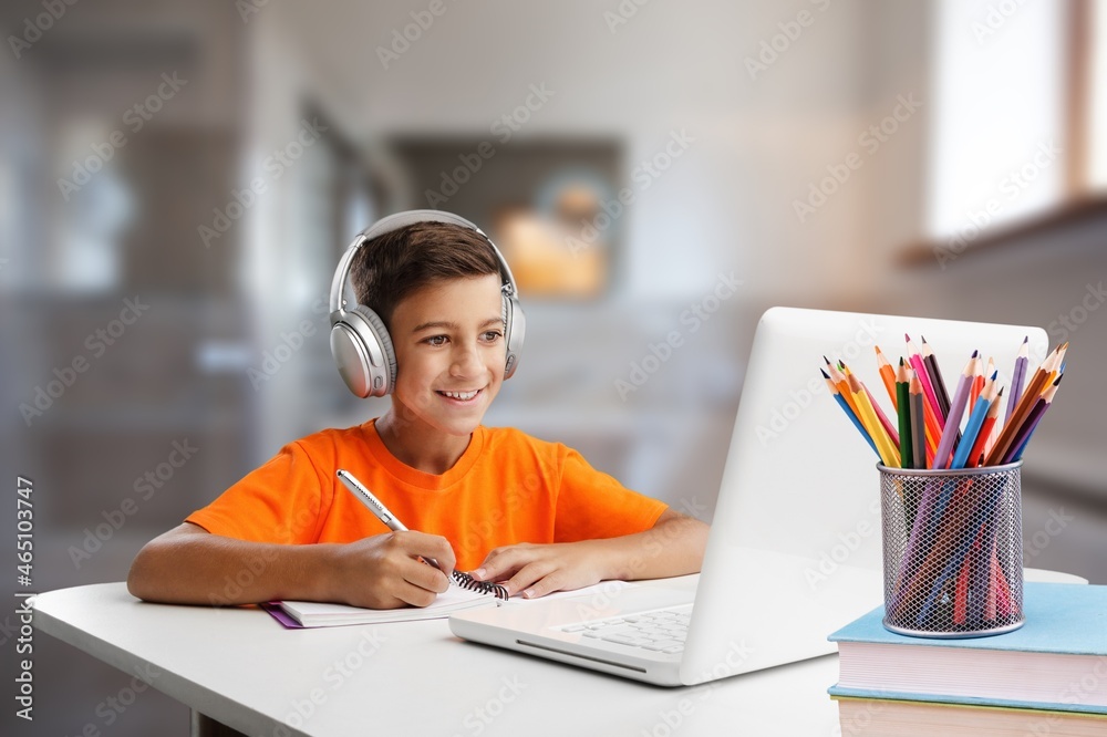 Little child using laptop and headphones studying at home,