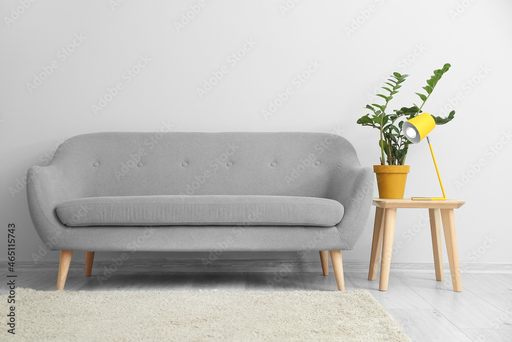 Table with yellow lamp, houseplant and sofa near light wall