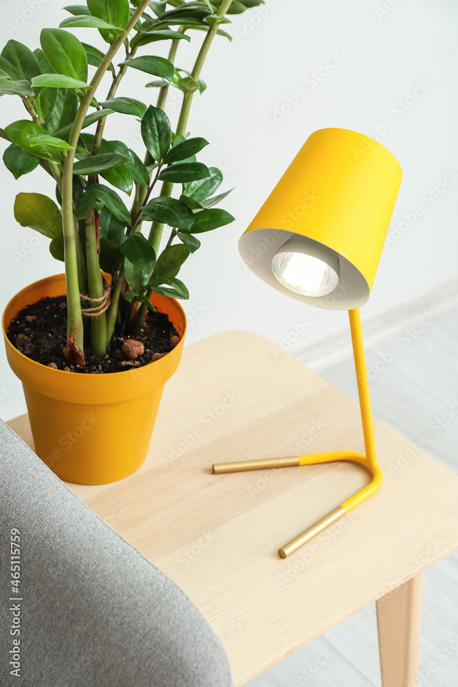 Table with yellow lamp and houseplant near light wall