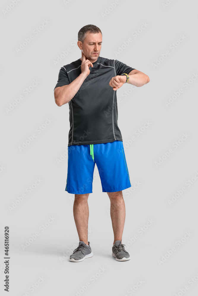 Male runner checking pulse on light background