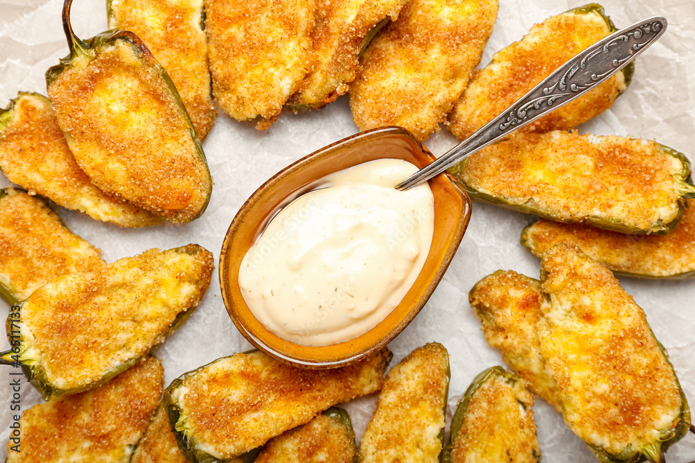 Parchment with tasty jalapeno poppers and sauce on table, closeup