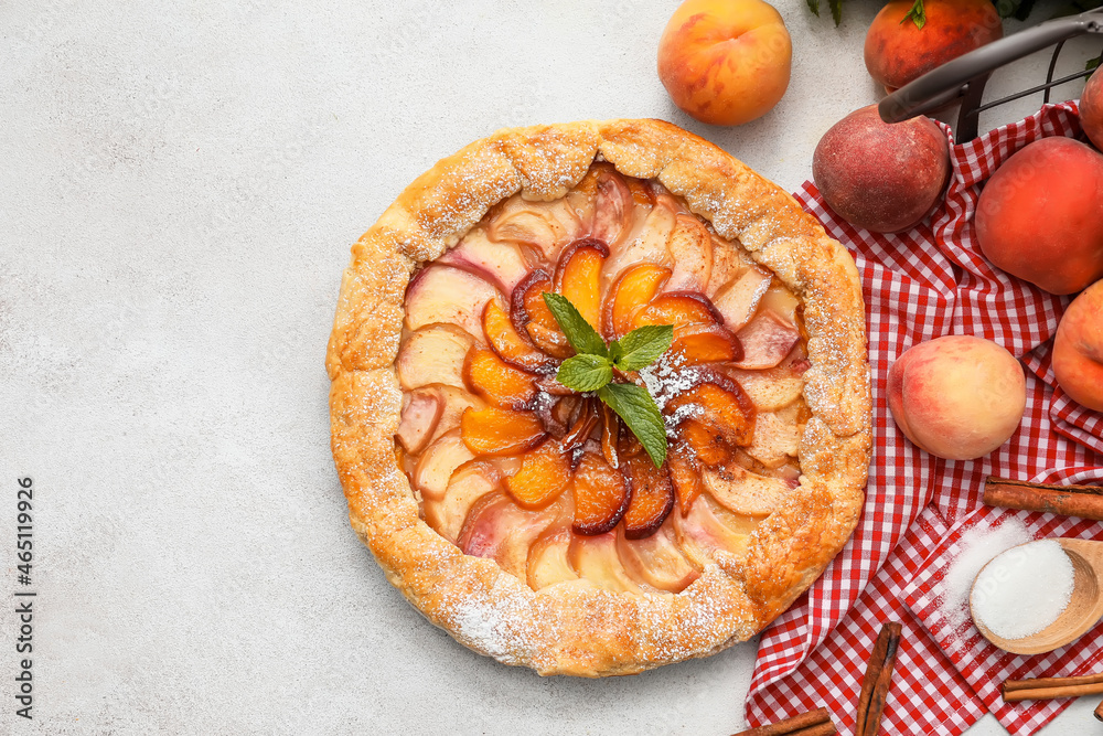 Tasty peach galette and cinnamon on light background