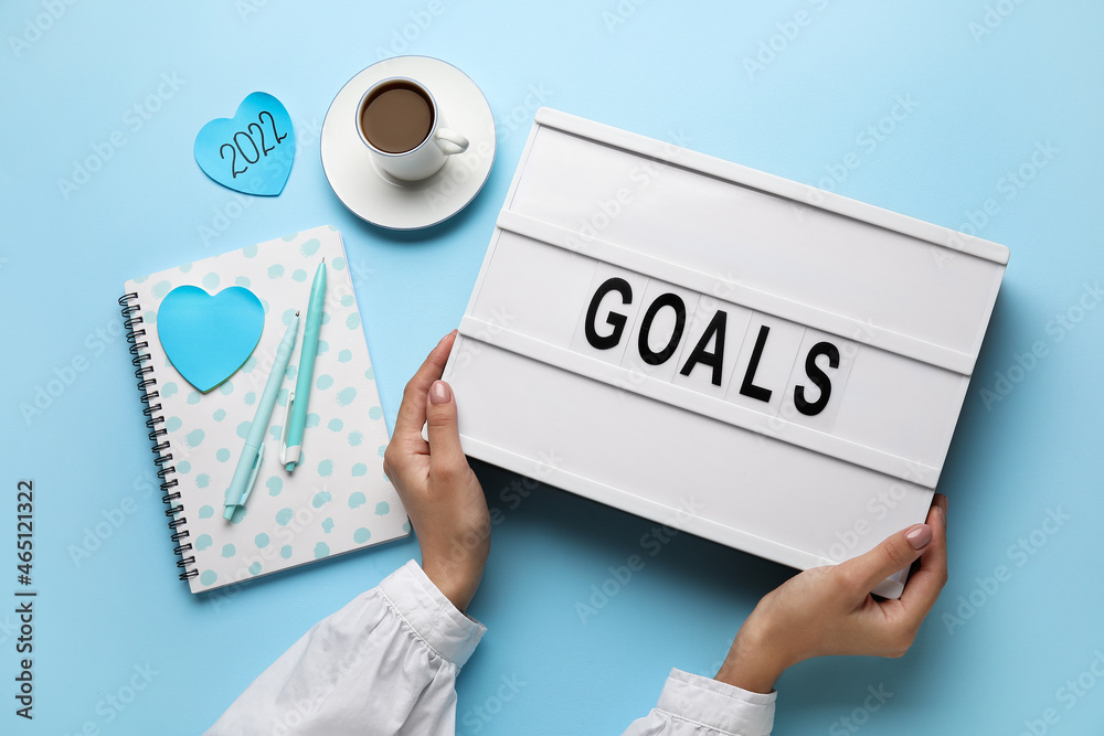 Female hands holding board with word GOALS on color background