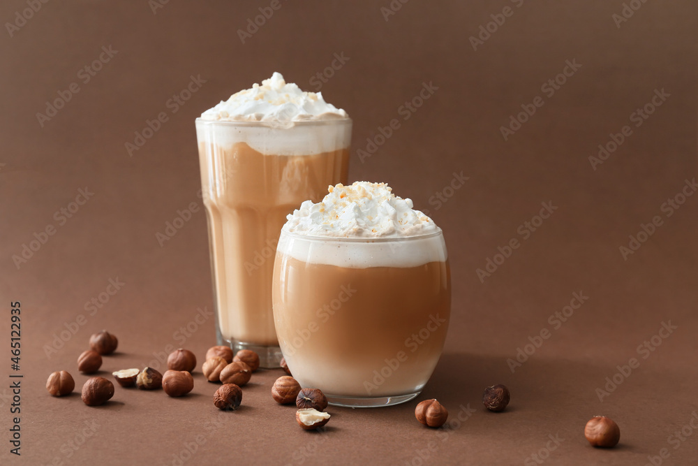 Glasses of tasty latte with nuts on brown background