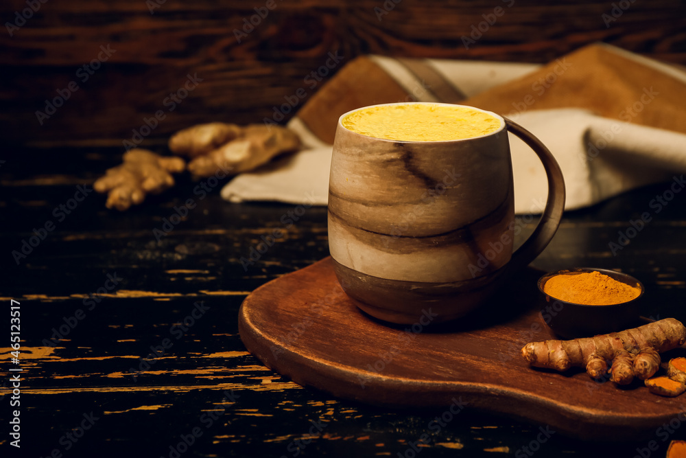 Cup of tasty homemade turmeric latte with powder on dark wooden