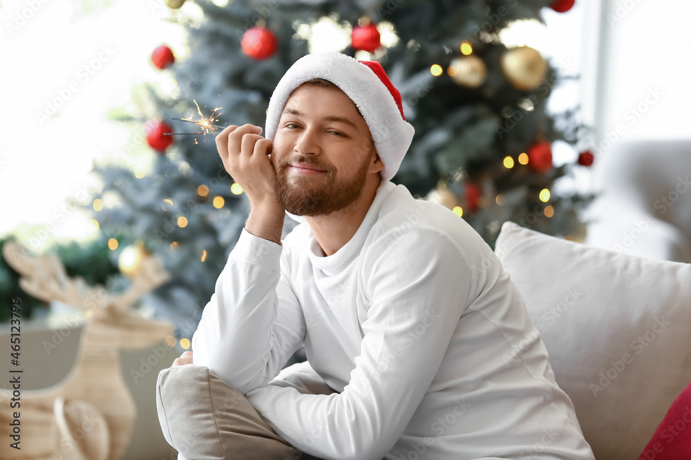 Young man in Santa hat with Christmas sparkler at home