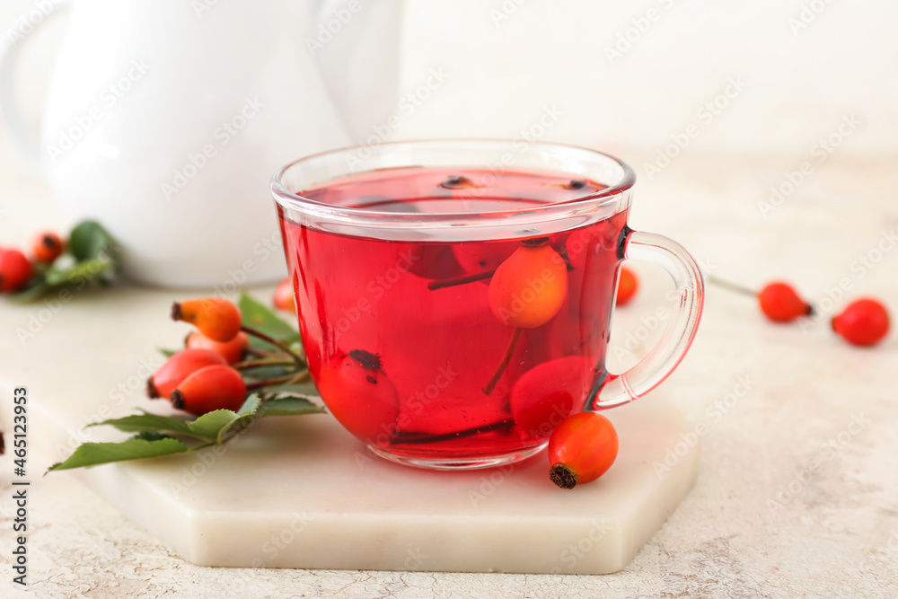 Glass cup of tasty rose hip tea and berries on light background