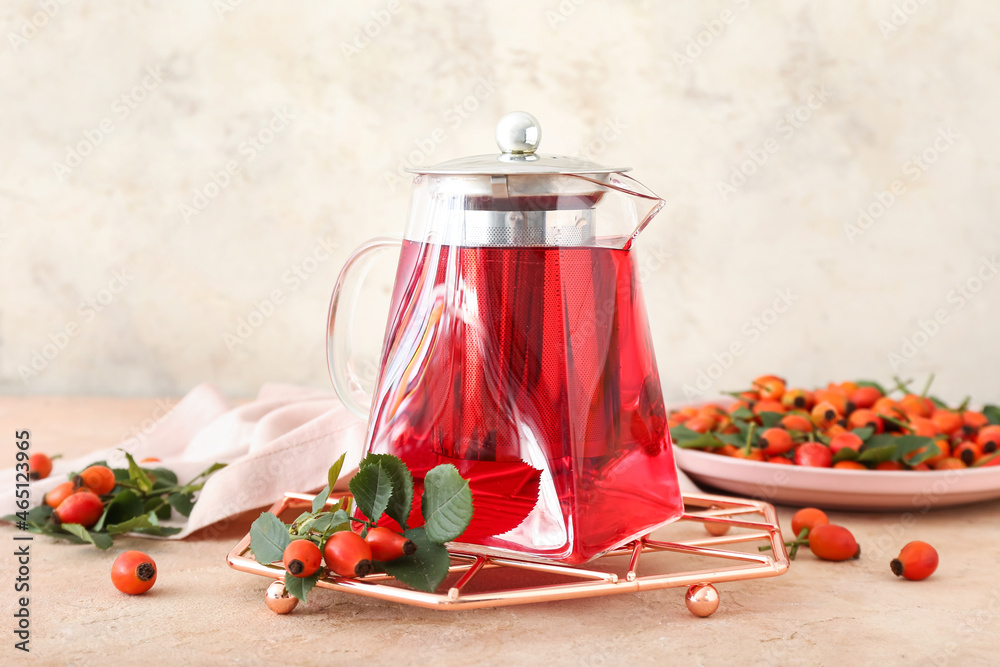 Tea pot of tasty rose hip beverage and berries on light background