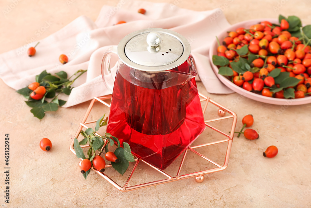 Tea pot of tasty rose hip beverage and berries on beige background