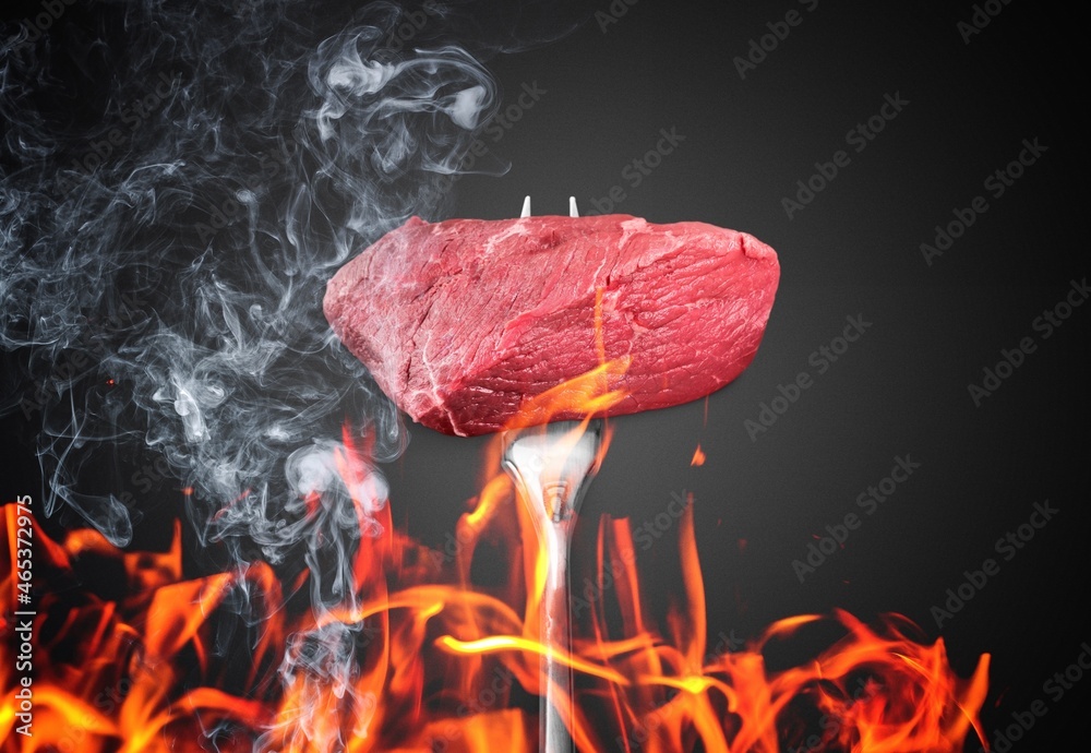 Hot medium rare steak on a dark background with fire and sparks.