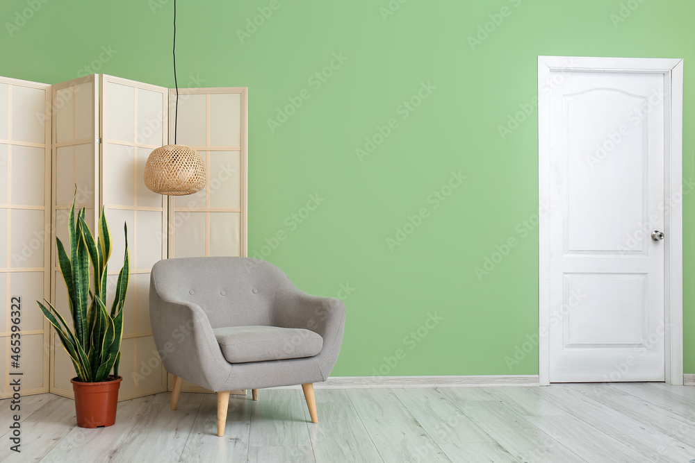 Grey armchair with houseplant and folding screen near green wall