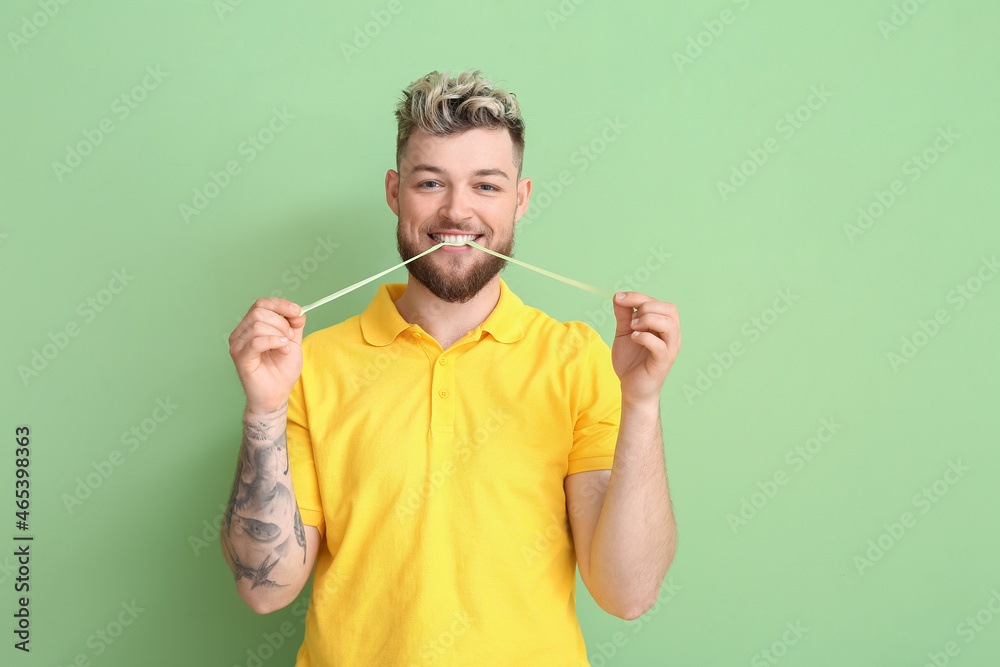 Funny young man with chewing gum on color background