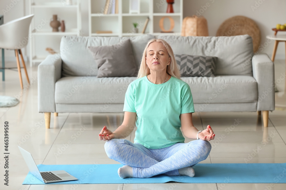 Beautiful mature woman meditating with laptop at home