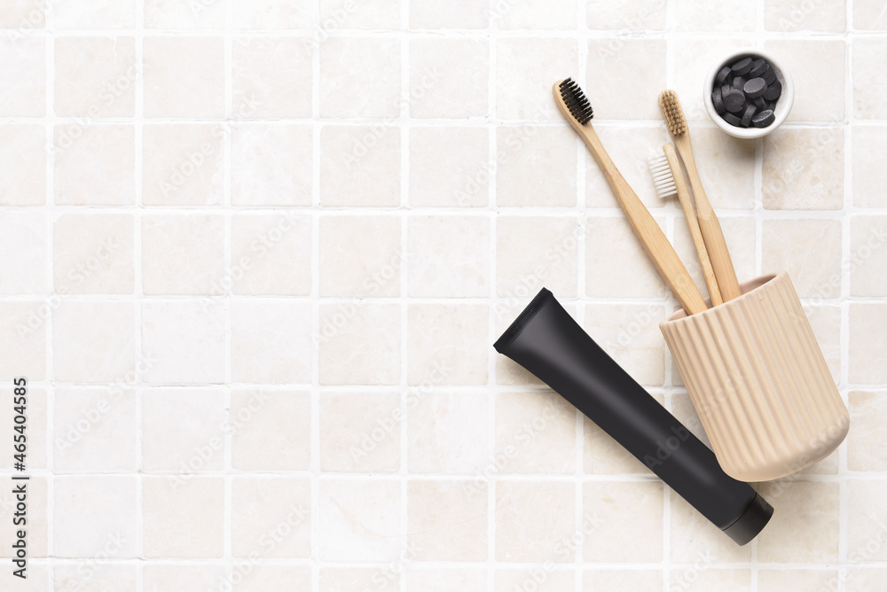 Black toothpaste with activated carbon, pills and brushes on bath tile background