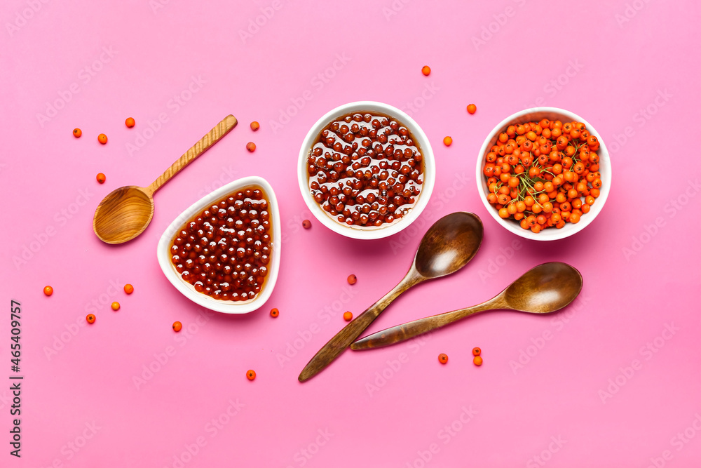 Composition with tasty rowan jam, berries and spoons on color background