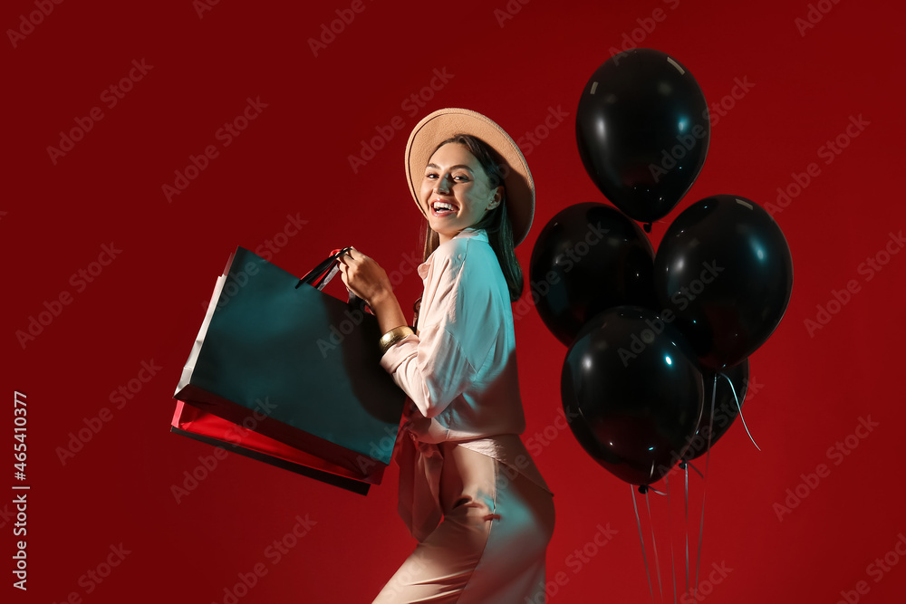 Happy young woman with shopping bags and balloons on color background. Black Friday sale