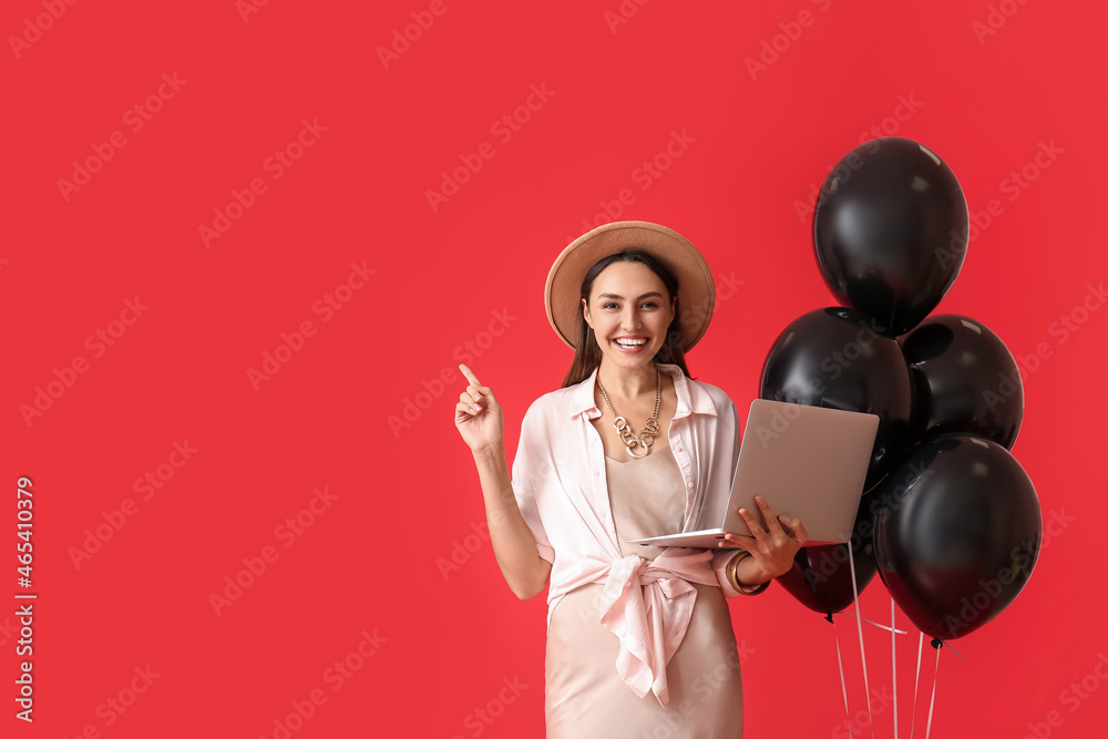 Happy young woman with laptop and balloons showing something on color background. Black Friday sale