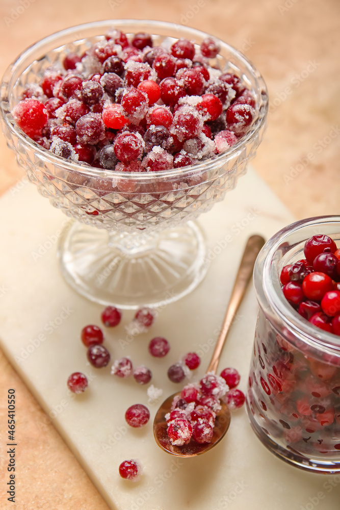 Glass bowl and jar with tasty sugared cranberries on beige background