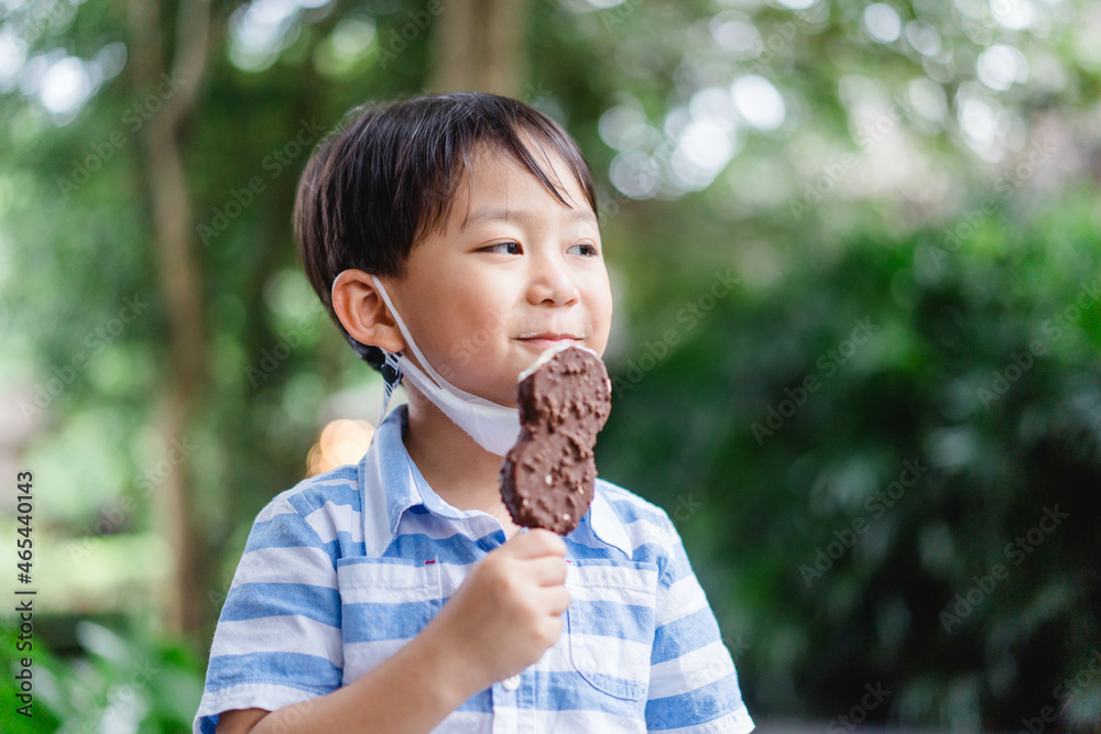 亚洲小孩蹒跚学步的男孩小孩在夏天户外自制的咬巧克力冰淇淋棒。美味