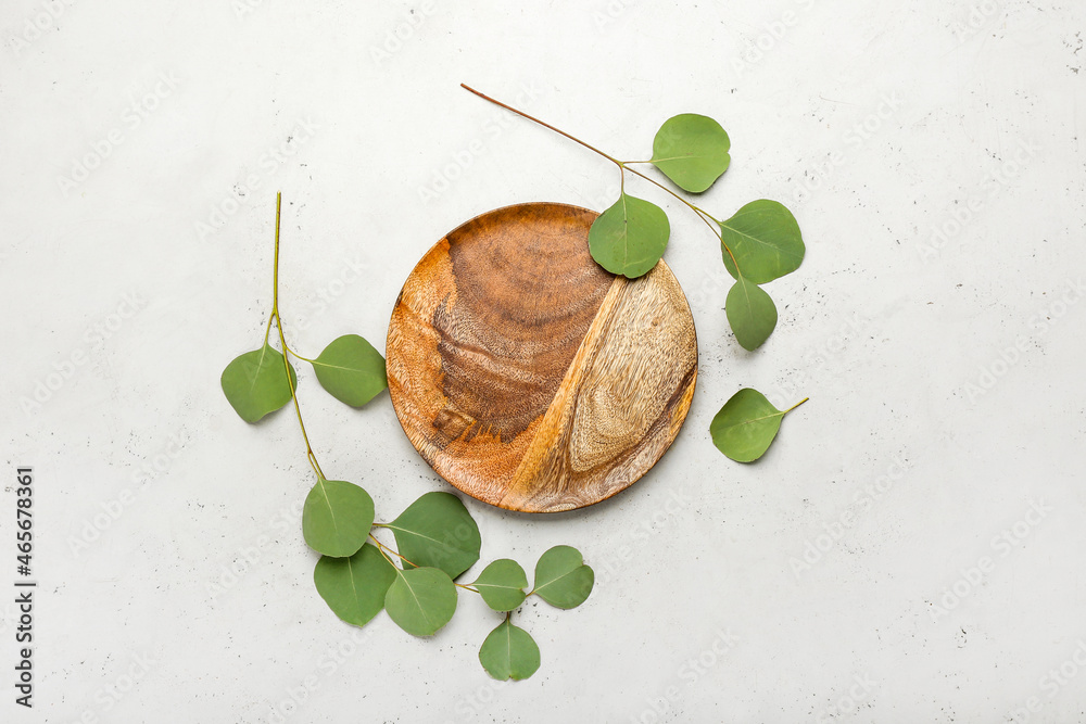 Wooden plate and eucalyptus branches on light background