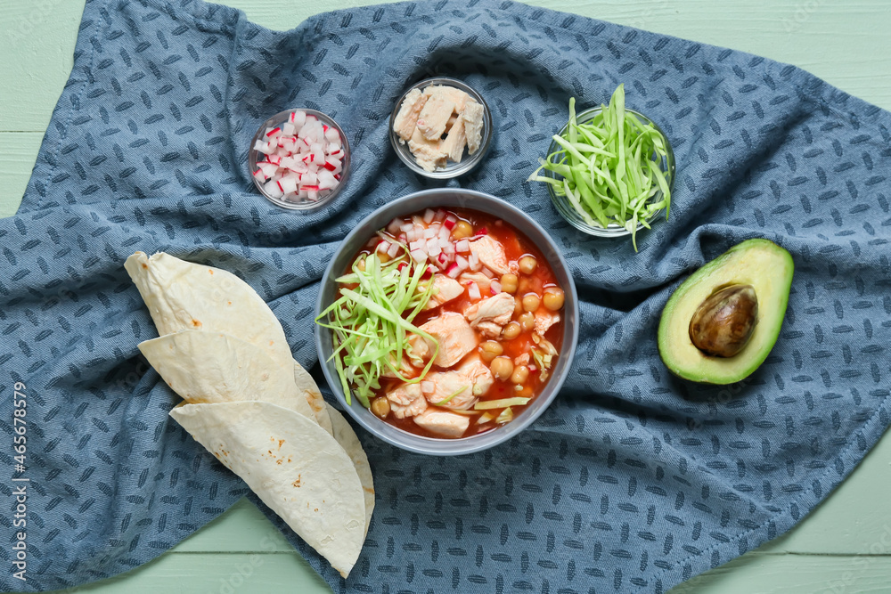 Bowl with tasty pozole soup and ingredients on color wooden background