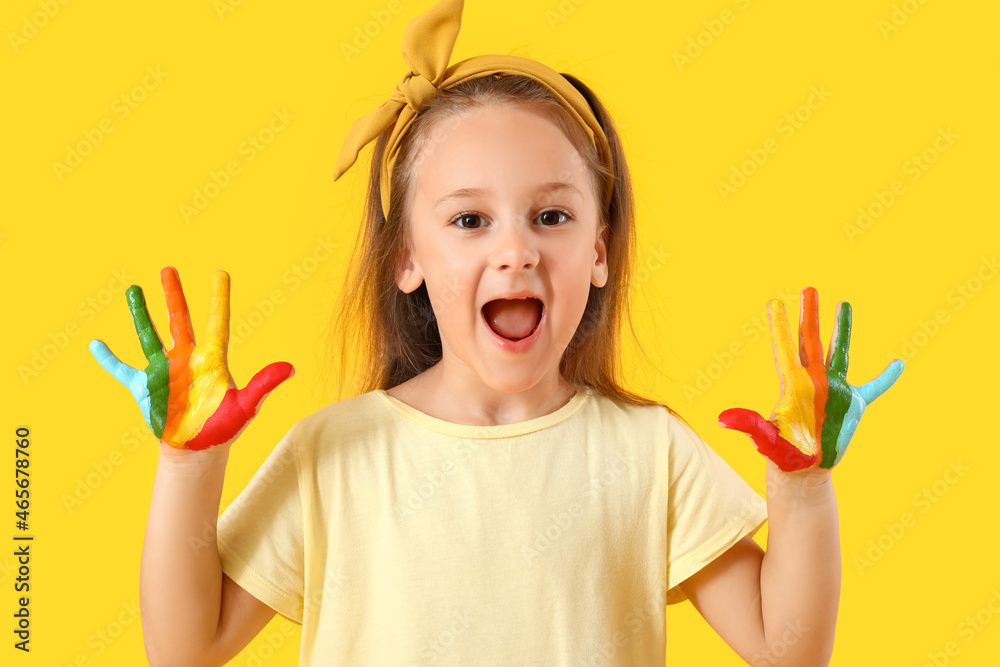 Cute little girl with hands in colorful paint on yellow background