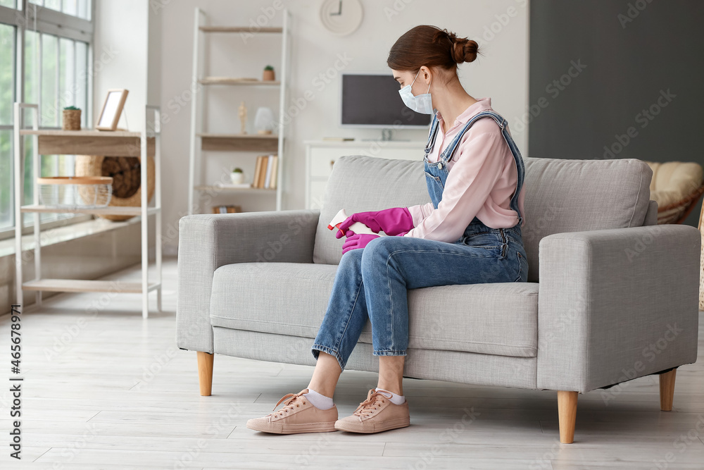 Woman in gloves cleaning grey sofa at home