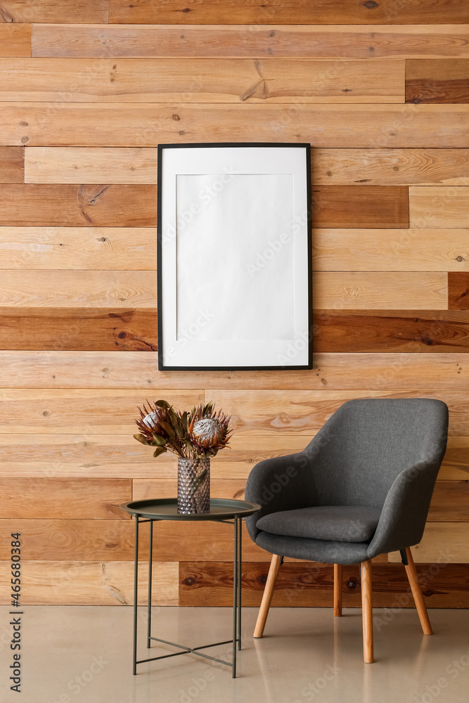 Blank poster frame on wooden wall in interior of modern room with armchair