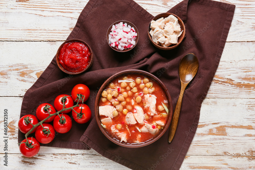 Bowl with tasty pozole soup and ingredients on light wooden background