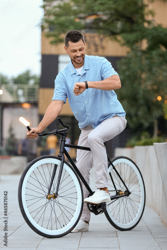 Man with bicycle looking at wrist watch on city street