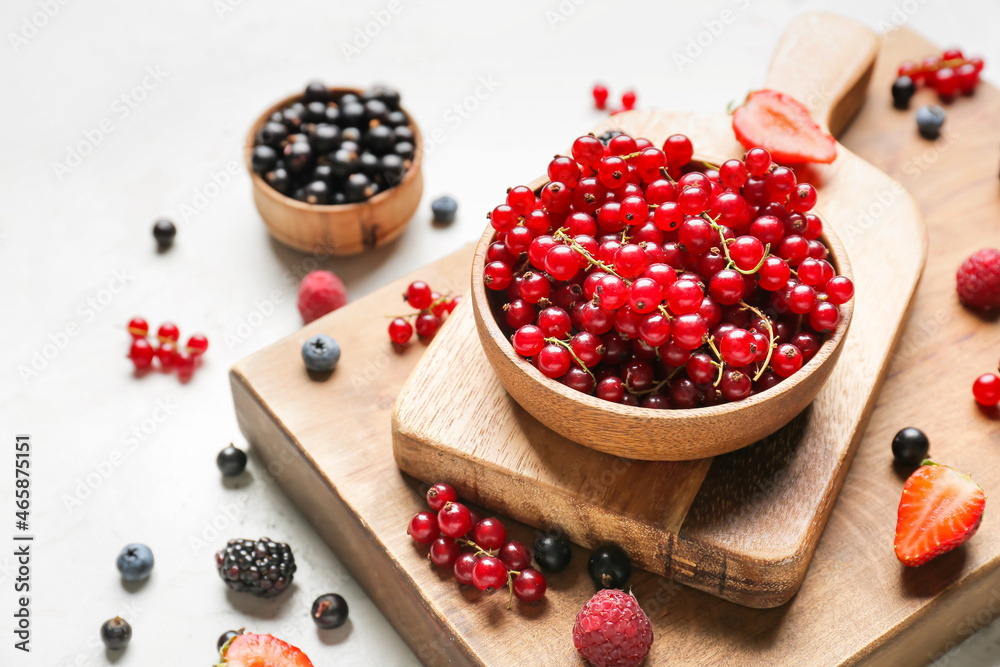 Bowl with tasty red currants and different berries on light background