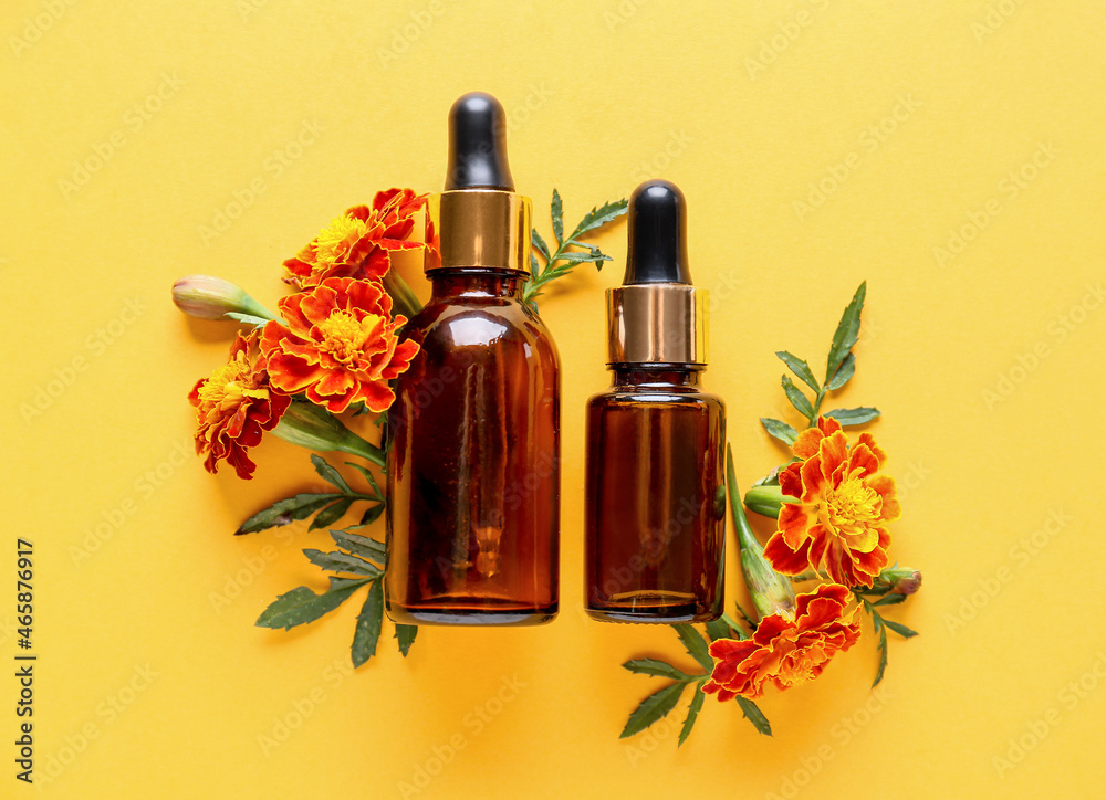 Bottles of essential oil and beautiful marigold flowers on color background