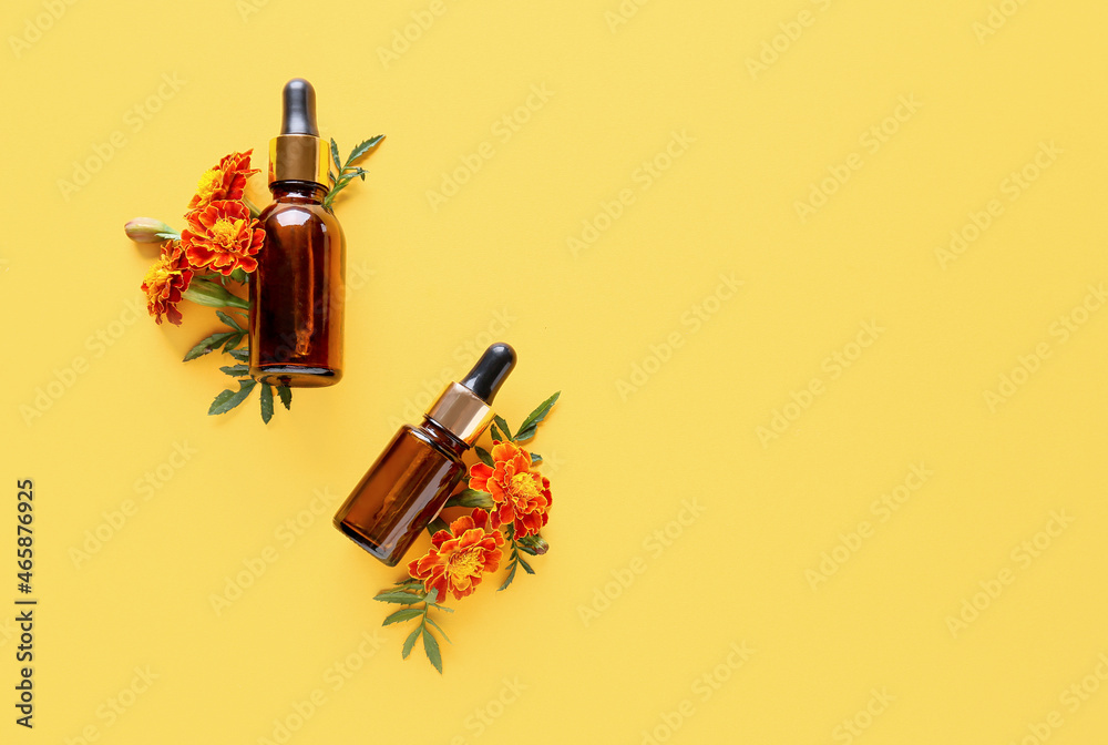 Bottles of essential oil and beautiful marigold flowers on color background