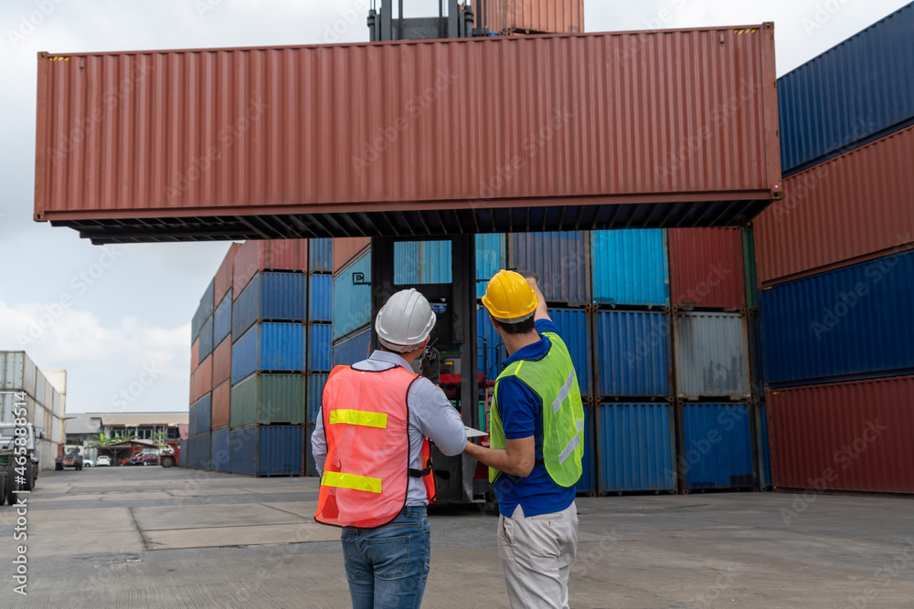 Industrial worker works with co-worker at overseas shipping container yard . Logistics supply chain 