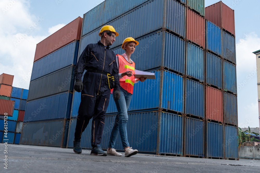 Industrial worker works with co-worker at overseas shipping container yard . Logistics supply chain 