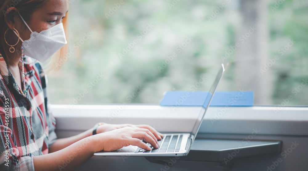 Businesswoman wearing a mask and working on laptop on a train, Asian freelance writer or designer wr