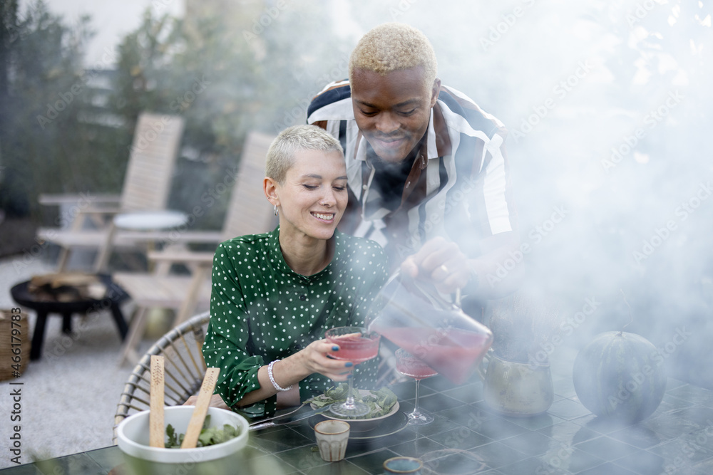 Black man taking juice for pouring in glass of his european girlfriend during dinner outdoors. Conce