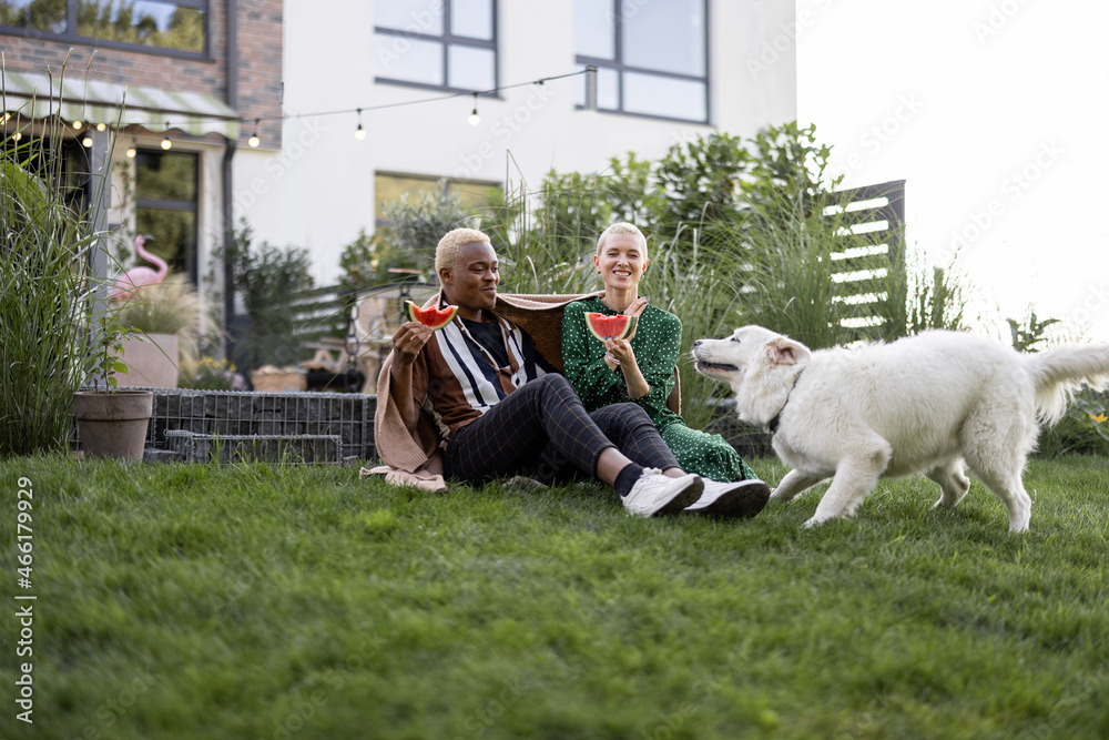 Multiracial couple eating watermelon in their garden. Concept of relationship and enjoying time toge