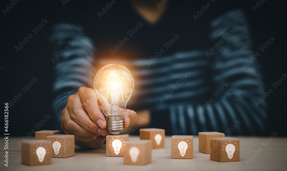 Man hand holding light bulb with Business icon on wood cube and working on desk, Creativity, and inn