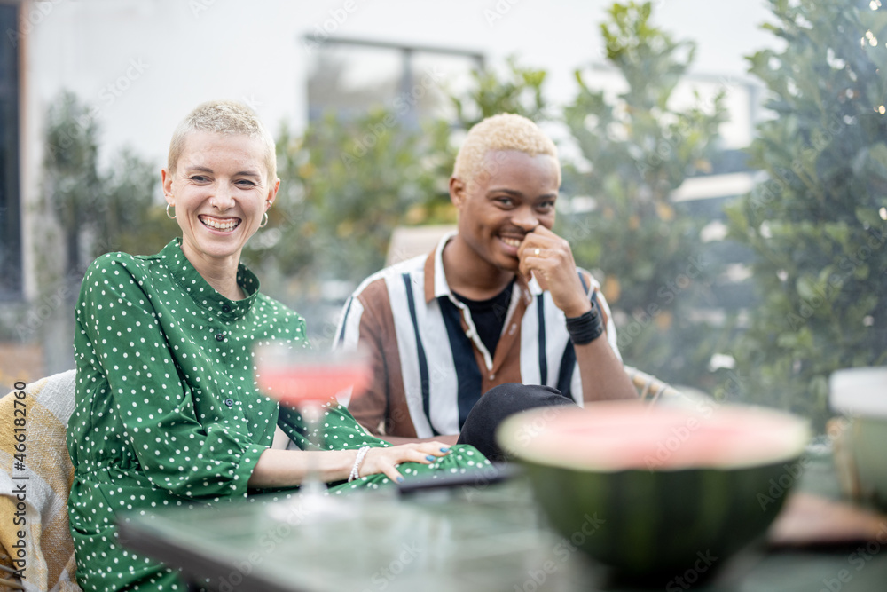 Multiracial couple talking and having fun during a dinnertime at their garden of country house. Idea