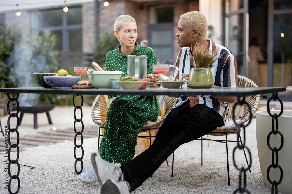 Multiracial couple talking and having fun during a dinnertime at their garden of country house. Idea