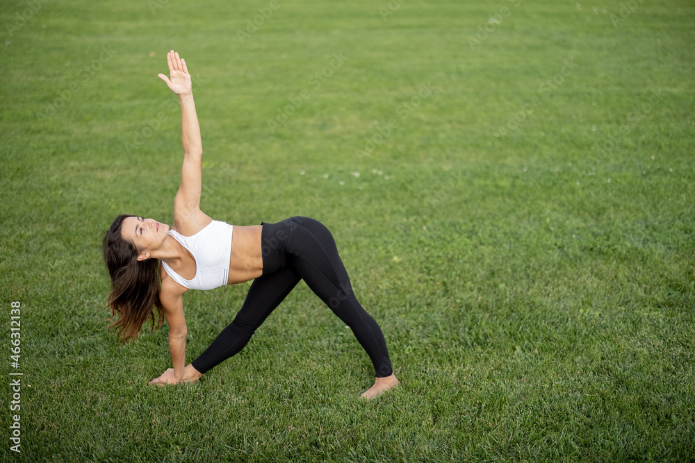 Young girl practicing yoga on green grass of meadow at sunny day. Concept of healthy lifestyle. Idea