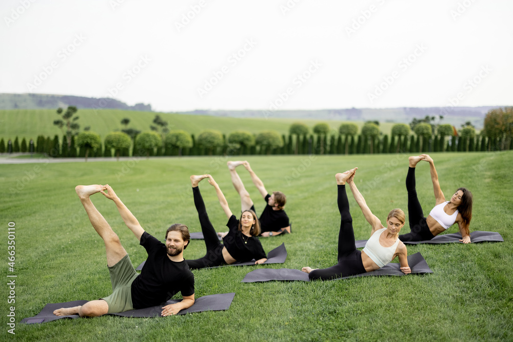 Group of european people practicing yoga on fitness mats on green meadow. Concept of healthy lifesty