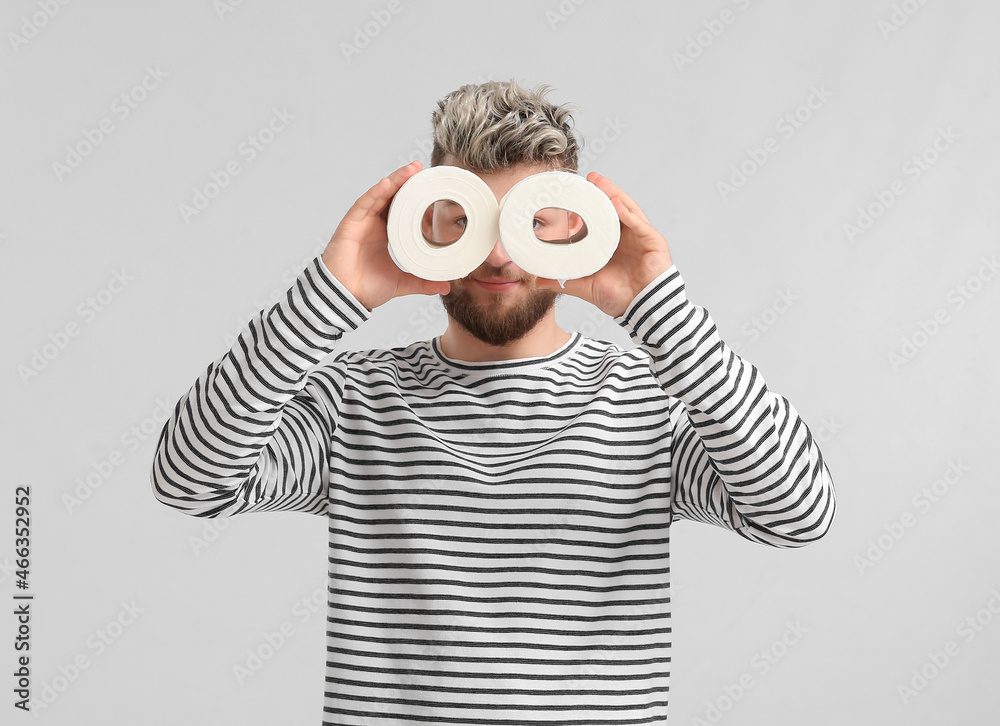 Funny young man with toilet paper on light background