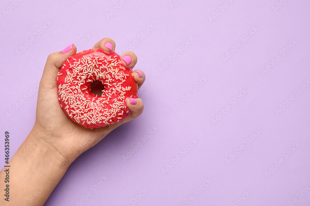 Woman with beautiful manicure holding delicious doughnut on purple background