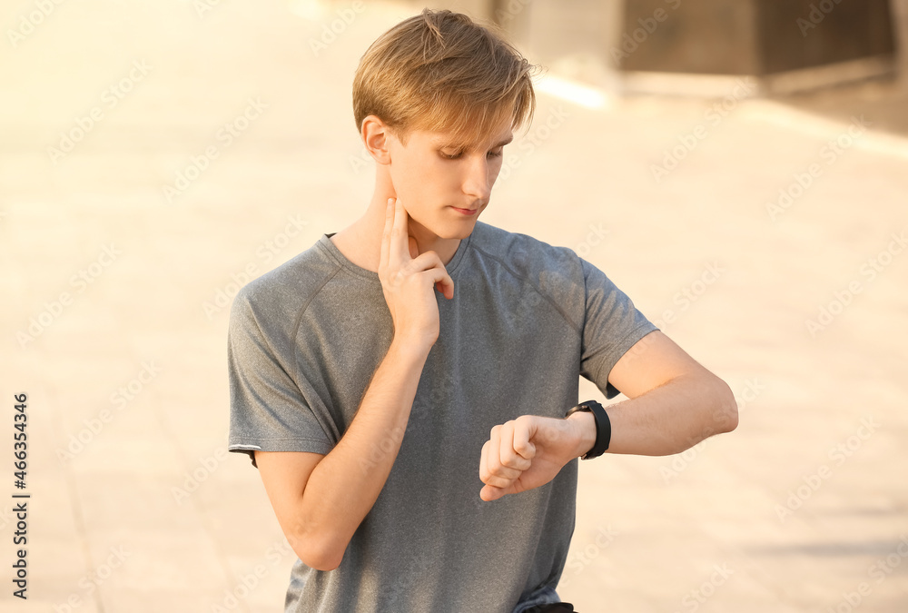 Sporty male runner checking pulse outdoors